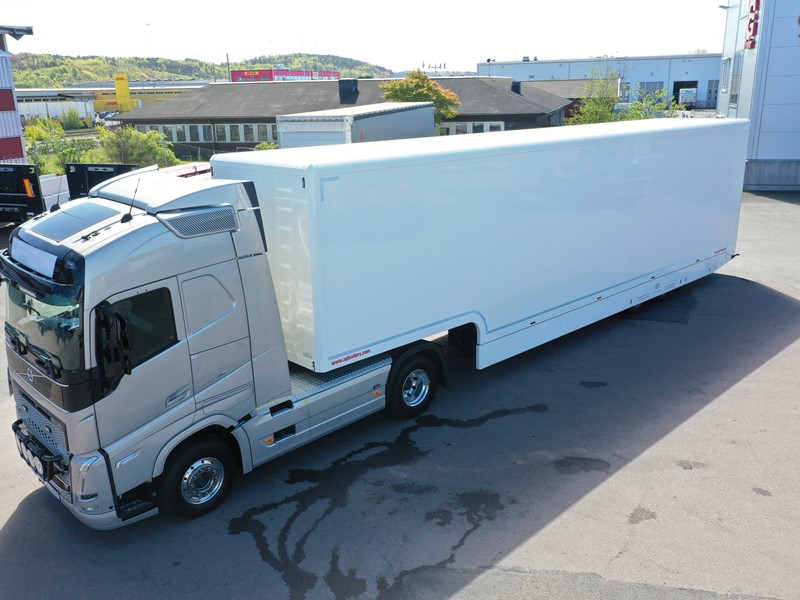 Vit racetrailer jumbo med påkopplad dragbil stående på asfaltsyta